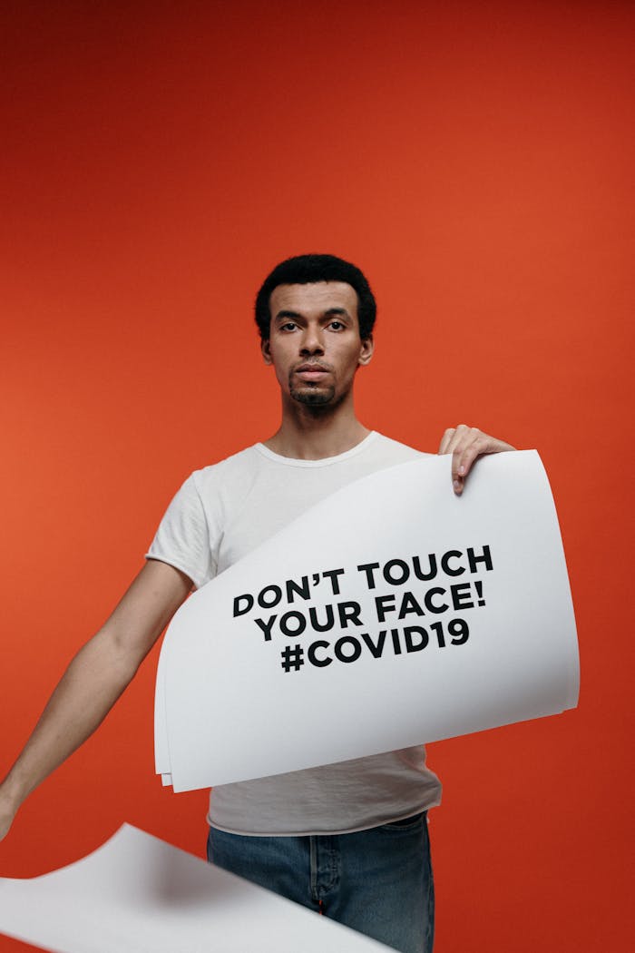 Man holding a sign that says Dont Touch Your Face! for COVID-19 awareness on a red background.